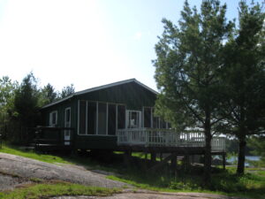 Front view of cottage six showcasing a green cottage with many windows and a deck